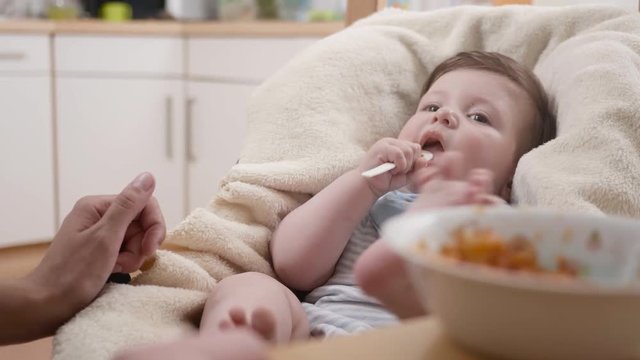 POV shot of a cute playful baby trying to put a spoon of baby food in his mouth.
