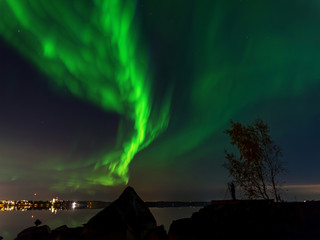 Fototapeta premium Northern lights over sea and a city in the background