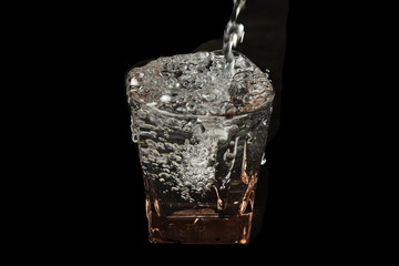 Water in glass with water splash on black background