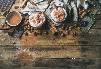 Warme chocolademelk met slagroom en kaneelstokjes geserveerd met anijssterren, verschillende noten en cacaopoeder op rustieke houten achtergrond, bovenaanzicht, selectieve aandacht, kopieerruimte, horizontale compositie