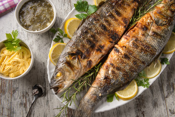 Due branzini cotti alla griglia su un piatto da portata e salsine