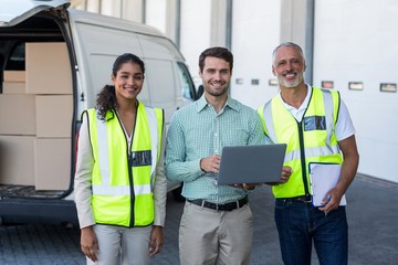 Manager and warehouse workers standing with laptop and clipboard