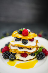 Delicious homemade pancakes with fresh ripe berries served on white plate on stone background. 