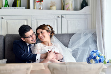 Wedding couple indoors is hugging each other. Beautiful model girl in white dress. Man in suit. Beauty bride with groom. Female and male portrait. Woman with lace veil. Cute lady and handsome guy