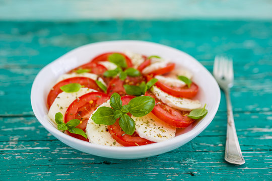 Delicious caprese salad with ripe tomatoes and mozzarella cheese with fresh basil leaves. Italian food.
