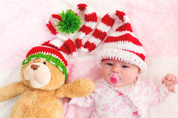 Baby girl in a Christmas hat with her teddy bear