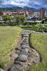 Stone walls of the ancient ruin city of Pumapungo, with the city of Cuenca, Ecuador, in the background, on a sunny morning