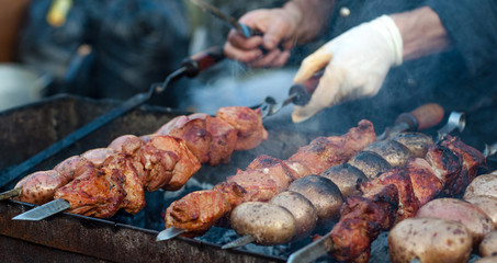 Male hand preparing meat and potatoes on grill
