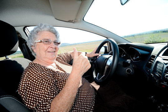 happy cheerful elderly senior woman driving her car showing thumbs up