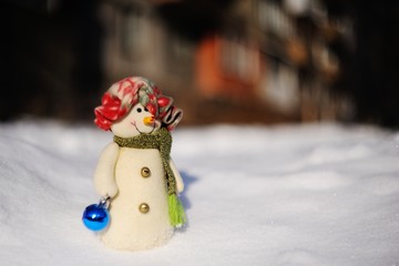 funny snowman in a hat with Christmas toys on a background of snow drifts