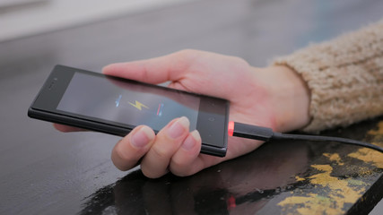 Woman's hand hold smartphone with low battery icon on screen - USB data cable connecting on modern gadget. Close up