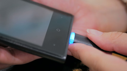 Woman's hand plugging black lightning charging cable into smartphone - USB data cable connecting on modern gadget. Close up