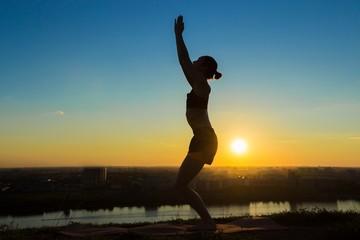 Fototapeta na wymiar Silhouette of sporty woman practicing yoga in the park at sunset. Sunset light, sun lens flares, golden hour. Freedom, health and yoga concept