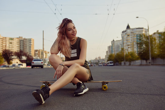 Beautiful young girl with tattoos sits on longboard