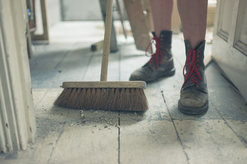 Young woman sweeping the floor - obrazy, fototapety, plakaty