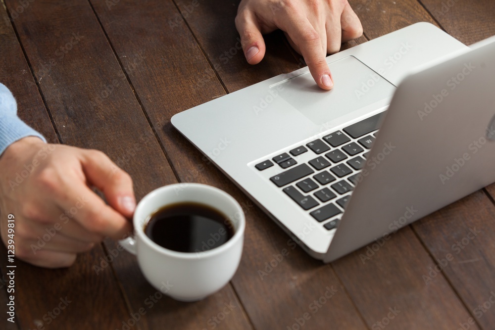 Poster man using laptop while having cup of coffee