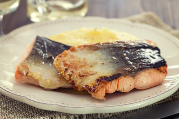 fried salmon with mashed potato on white dish on brown wooden background