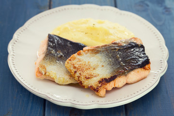 fried salmon with mashed potato on white dish on blue wooden background