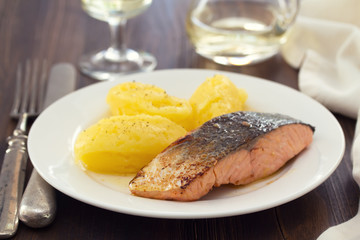 fried salmon with mashed potato on white dish on brown wooden background