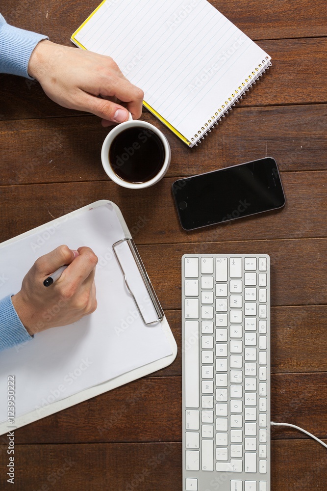 Poster man writing on clipboard while having cup of coffee