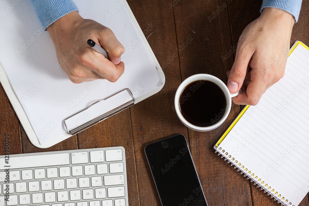 Poster man writing on clipboard while having cup of coffee