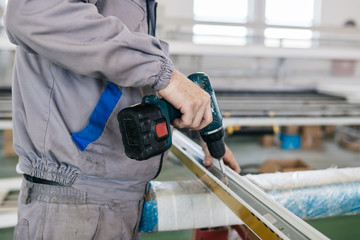 Factory for aluminum and PVC windows and doors production. Manual worker assembling PVC doors and windows and working with screw gun.