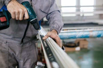 Factory for aluminum and PVC windows and doors production. Manual worker assembling PVC doors and windows and working with screw gun. 