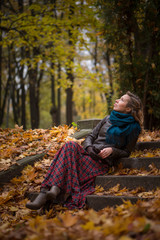 Beautiful girl blonde with wavy hair sitting in the park on autumn leaves 