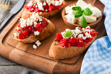Bruschetta with tomatoes, feta cheese and basil. Traditional Greek snack on wooden background. Selective focus.