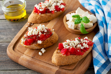 Bruschetta with tomatoes, feta cheese and basil. Traditional Greek snack on wooden background. Selective focus.