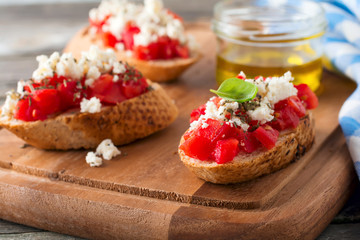 Bruschetta with tomatoes, feta cheese and basil. Traditional Greek snack on wooden background. Selective focus.