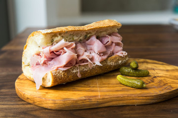 Ham baguette sandwich with pickles on a wood cutting board