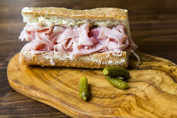 Ham baguette sandwich with pickles on a wood cutting board