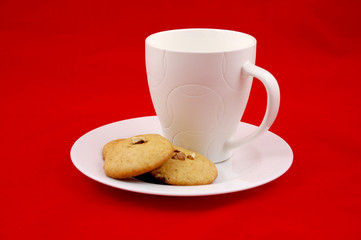 Milk and cookies. A mug of milk and a few home made ginger bread and walnuts cookies on a plate, isolated on red background.Christmas morning. 