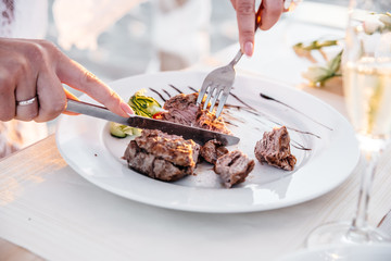 Juicy beef steak, fork and knife with woman's fingers with french manicure