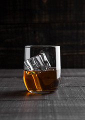 Glass of whiskey with ice on wooden background