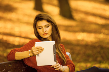 Woman on bench in park with tablet.