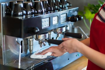 Waitress wiping espresso machine with napkin in café