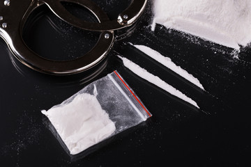 Handcuffs and cocaine on black background