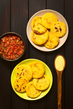 Colombian Arepa cornmeal patties with hogao sauce (tomato and onion cooked), photographed overhead on dark wood with natural light.