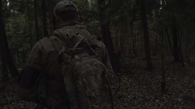Soldier with a gun in his hand goes through the dark forest
