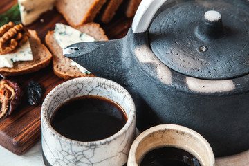 Old ceramic kettle with two cups of tea and sandwiches on a wooden background