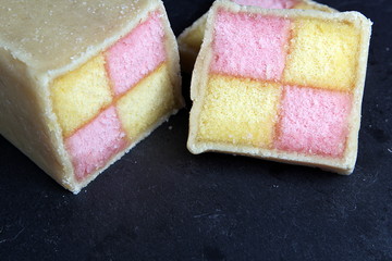 Freshly cut Battenberg Cake on dark slate board. Pink and yellow sponge covered in marzipan