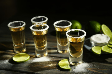 Gold tequila shots with lime and salt on wooden table
