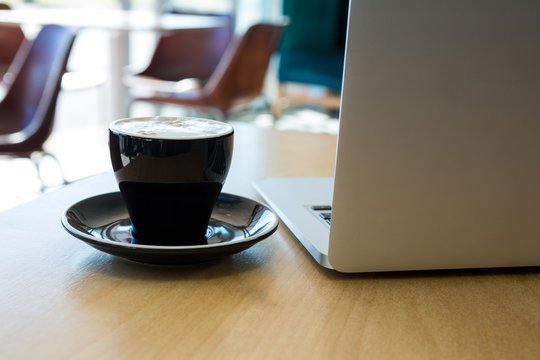Close -up of cup of coffee and laptop on table