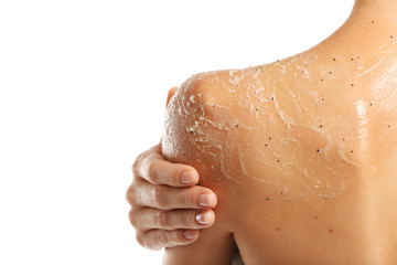 Young woman applying scrub on shoulder on white background