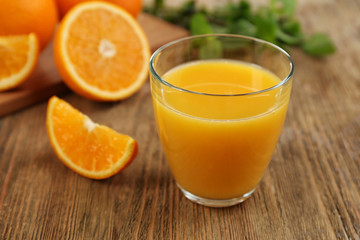 Juice in glass and oranges on wooden table