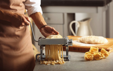 Man using pasta machine to prepare tagliatelle, close up view