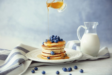 Pouring honey from gravy boat on stack of delicious pancakes with blueberries