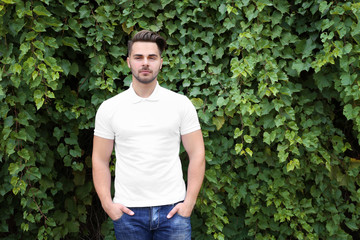 Naklejka na ściany i meble Young man in blank polo shirt on green leaves background